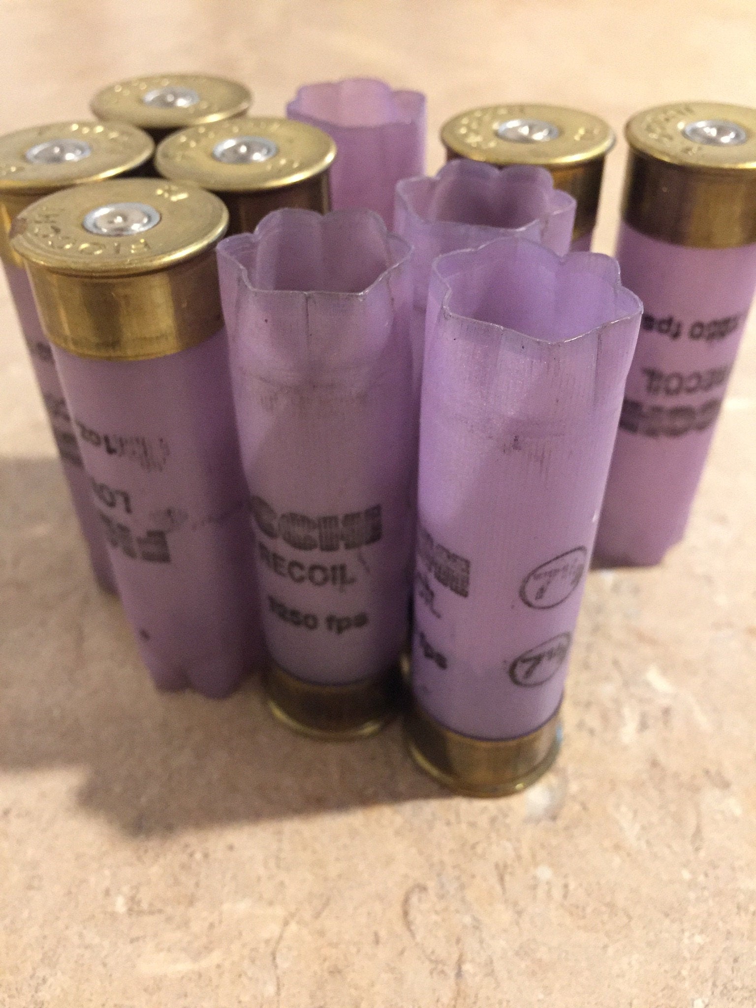Group of purple Fiocchi Low Recoil 12 gauge shotgun shells, some with crimped star-fold tops and some with brass base caps, on a tile surface