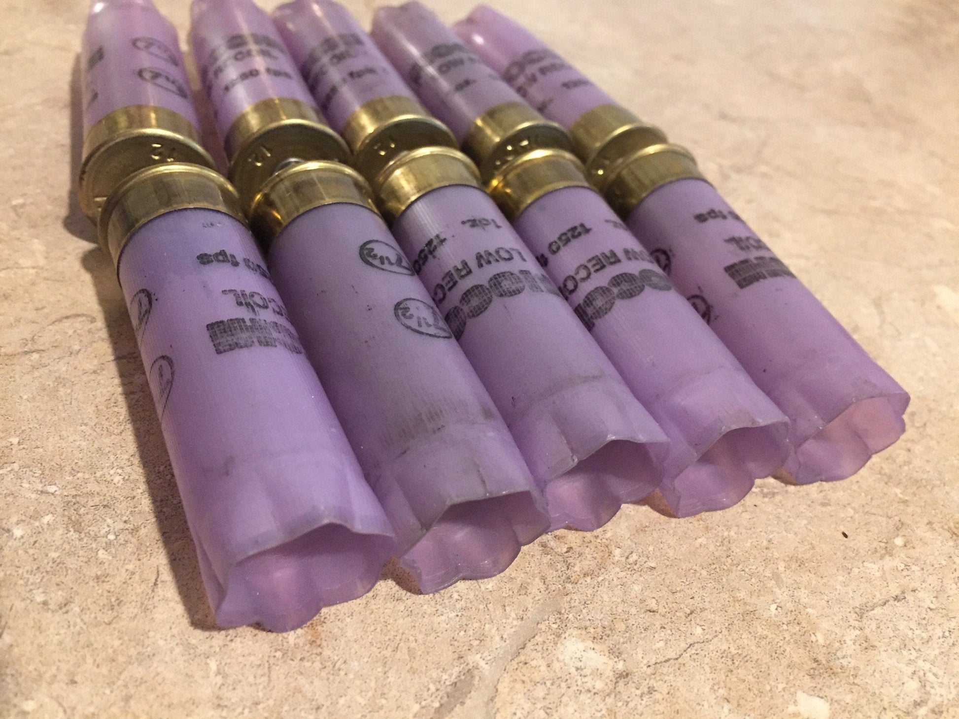 5 purple Fiocchi Low Recoil 12 gauge shotgun shells with brass bases, lying on a tile surface