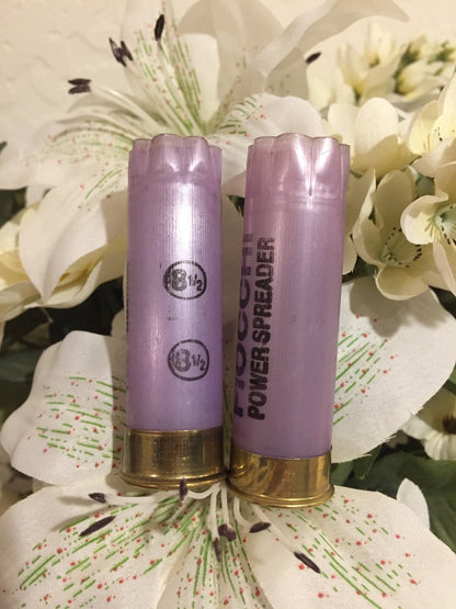 2 purple Fiocchi Power Spreader 12 gauge shotgun shells with brass bases, standing among white lily flowers