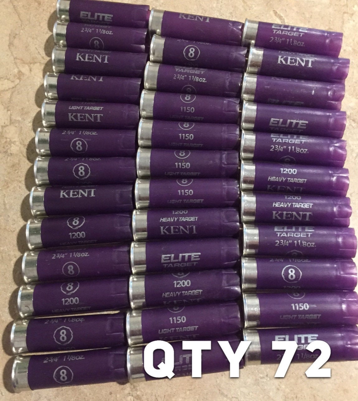 Rows of purple Kent Elite Target 12 gauge shotgun shells with silver heads on a stone surface, text reading QTY 72