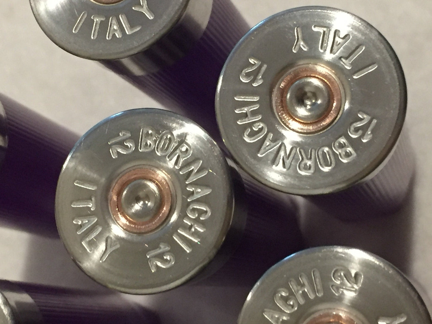 Close-up of silver-colored headstamps on purple empty 12-gauge shotgun shell hulls