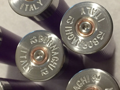 Close-up of silver-colored headstamps on purple empty 12-gauge shotgun shell hulls