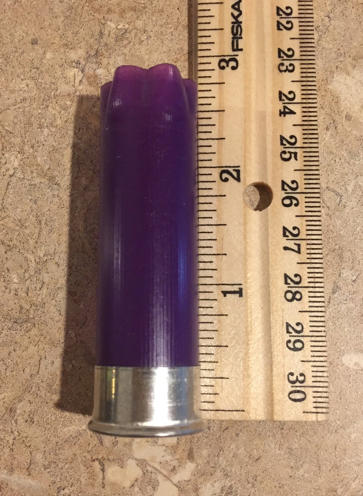 Purple empty 12-gauge shotgun shell hull beside a ruler for size reference