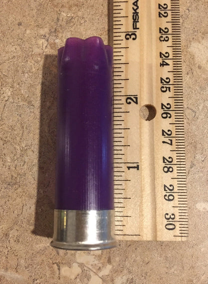 Purple empty 12-gauge shotgun shell hull beside a ruler for size reference