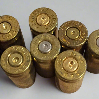 Six raw 9mm brass casings standing upright displaying legible headstamps and indented primers.