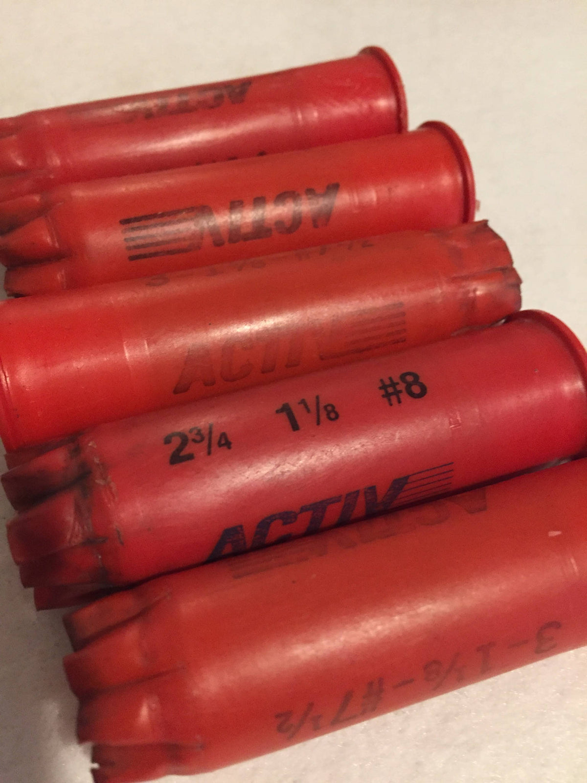 5 red plastic shotgun shells lying in a row printed "Activ", "2¾ 1⅛ #8", and "3-1⅛-#7½" text
