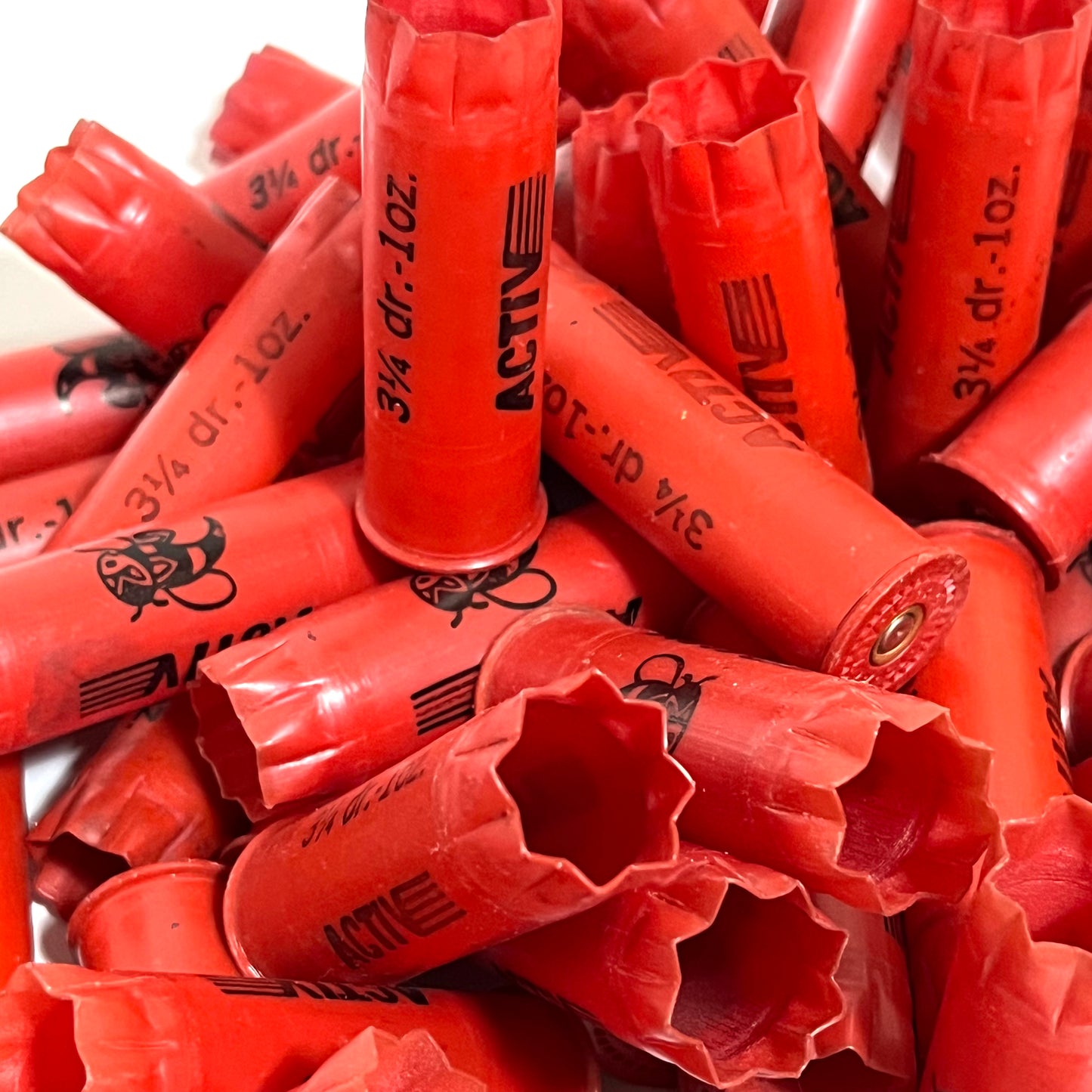 Pile of red plastic shotgun shells printed "Activ" and "3¼ dr.-1oz." text, viewed close-up