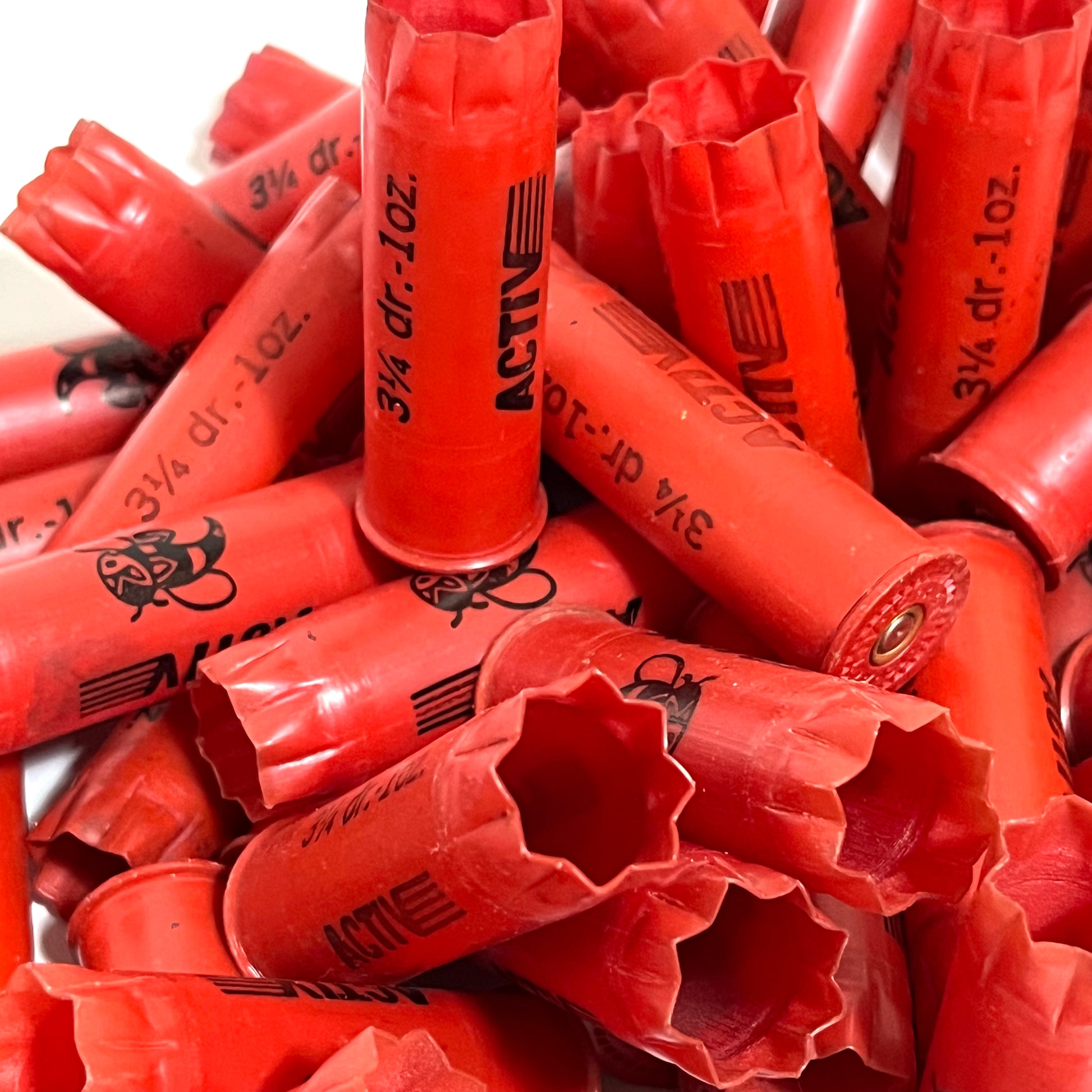 Pile of red plastic shotgun shells printed "Activ" and "3¼ dr.-1oz." text, viewed close-up