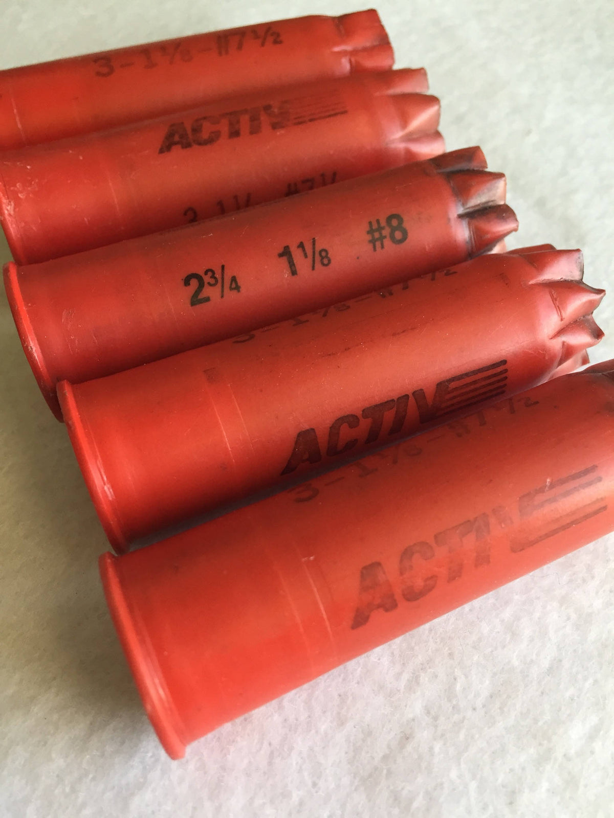 5 red plastic shotgun shells lying at angles printed "Activ", "3-1⅛-#7½", and "2¾ 1⅛ #8" text