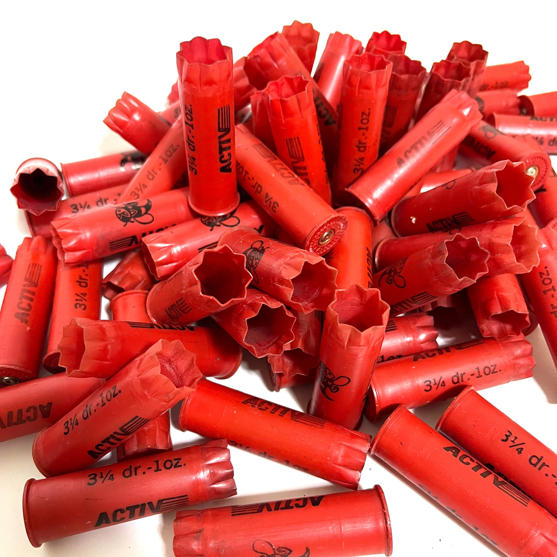 Pile of red plastic shotgun shells printed "Activ" and "3¼ dr.-1oz." text, some showing open star-crimped mouths