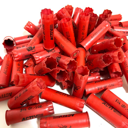 Pile of red plastic shotgun shells printed "Activ" and "3¼ dr.-1oz." text, some showing open star-crimped mouths