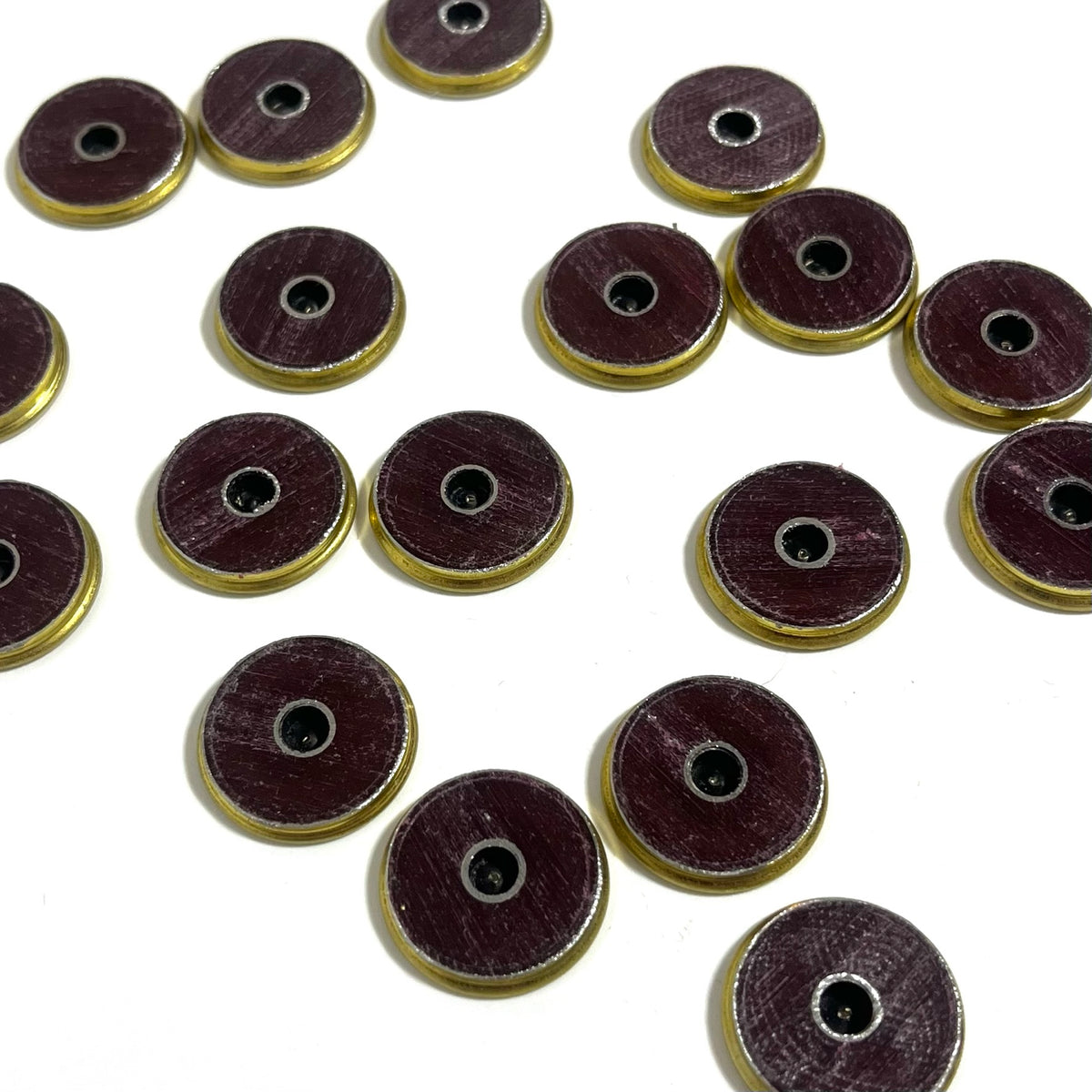 17 dark maroon shotgun shell slices with brass rims and drilled centers scattered on a white background