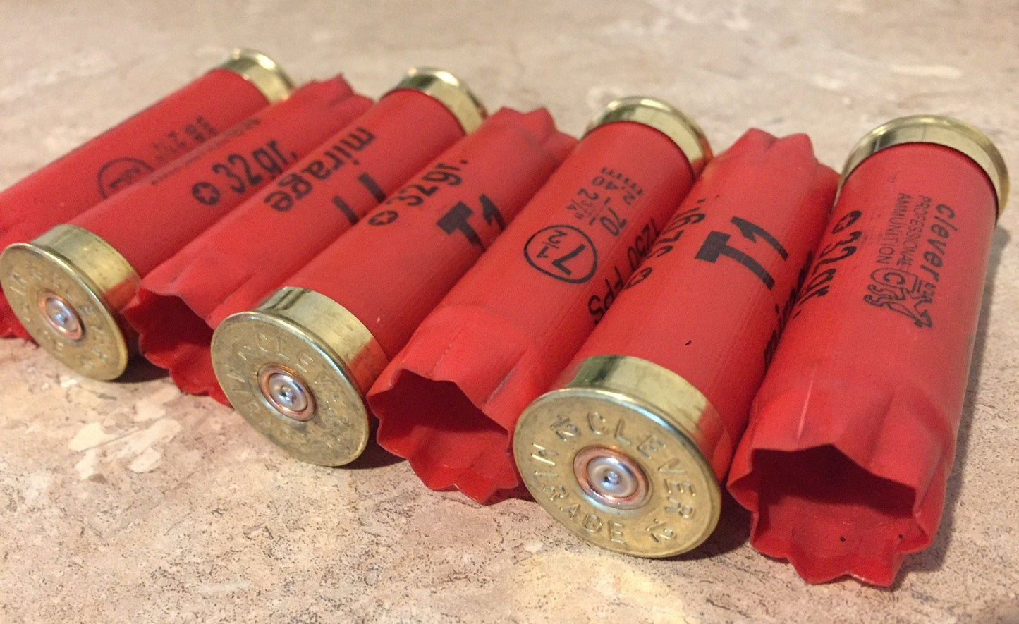 Six red Clever Mirage T1 12 gauge shotgun shells with gold headstamps lying in a row