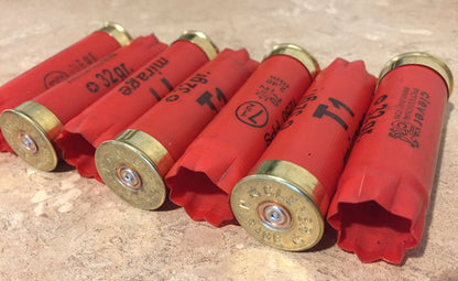 Six red Clever Mirage T1 12 gauge shotgun shells with gold headstamps lying in a row