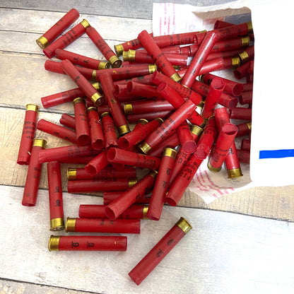 Large pile of empty red 410 bore shotgun shells with brass bases spilling out of a cardboard shipping box