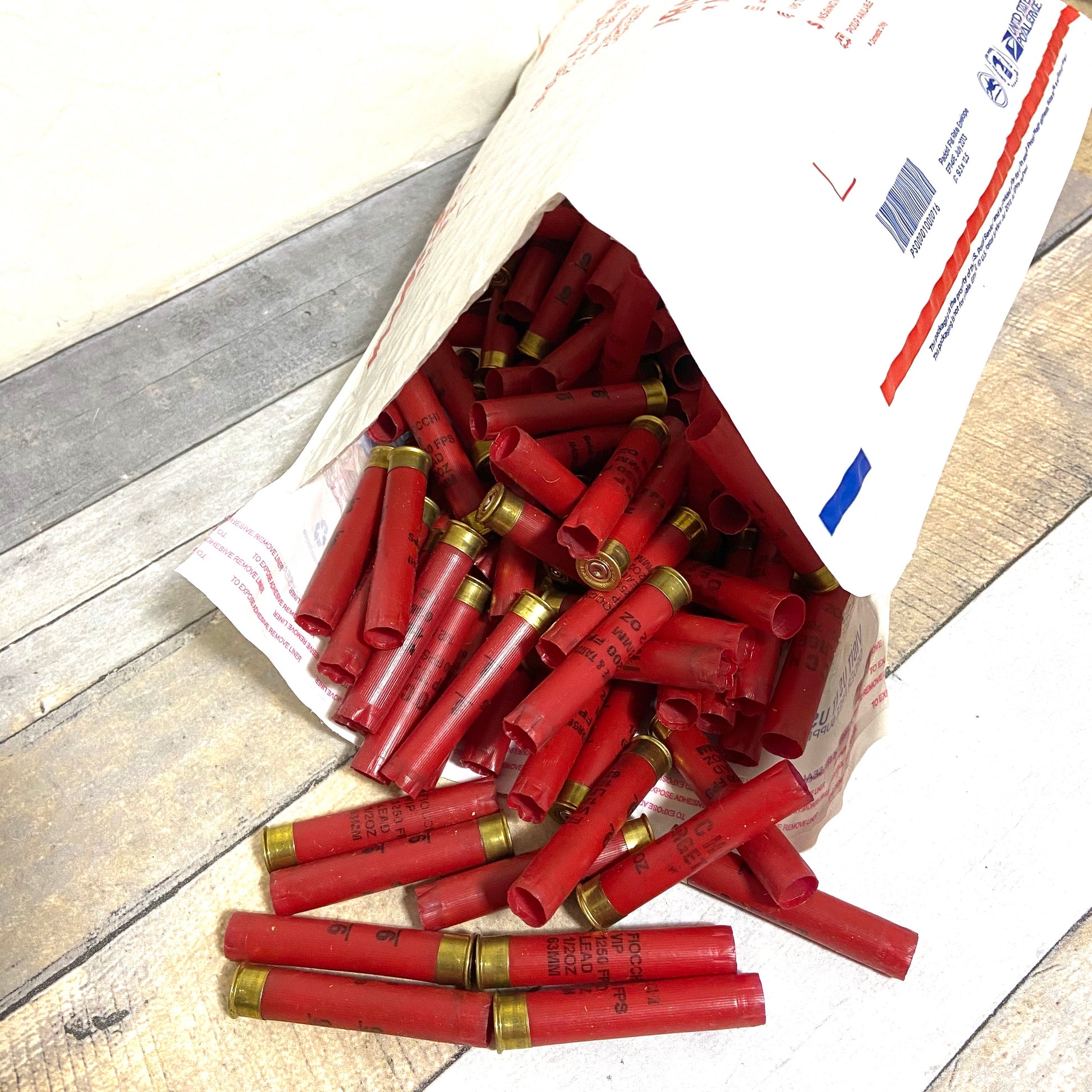 Large pile of empty red 410 bore shotgun shells with brass bases spilling out of a paper mailing envelope