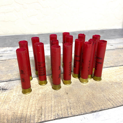 Group of empty red 410 bore shotgun shells with brass bases standing on a wood deck