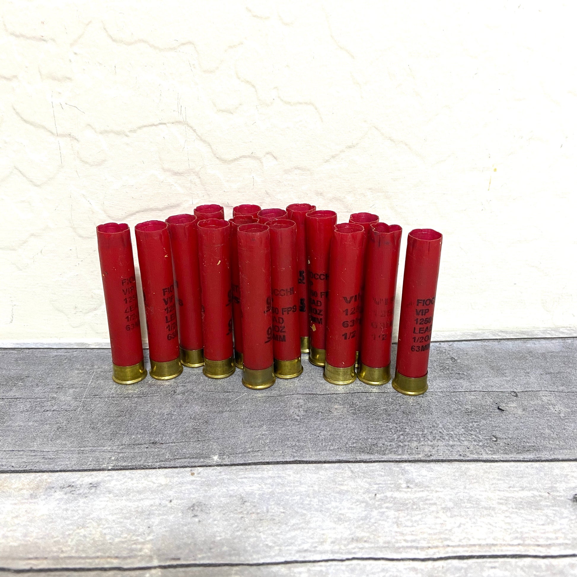 Group of empty red 410 bore shotgun shells with brass bases standing against a wall on a wood deck