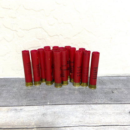 Group of empty red 410 bore shotgun shells with brass bases standing against a wall on a wood deck