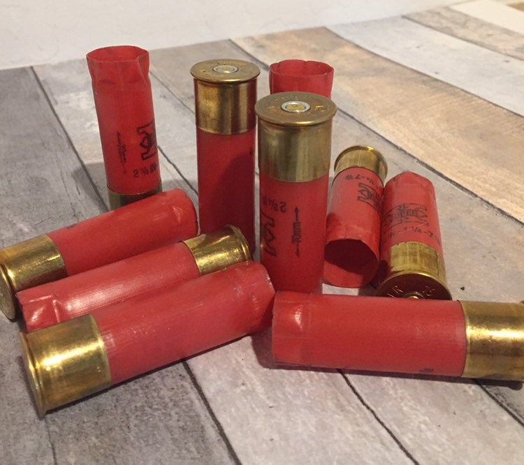 Group of red 12 gauge empty shotgun shells with gold bases scattered on a wood plank surface