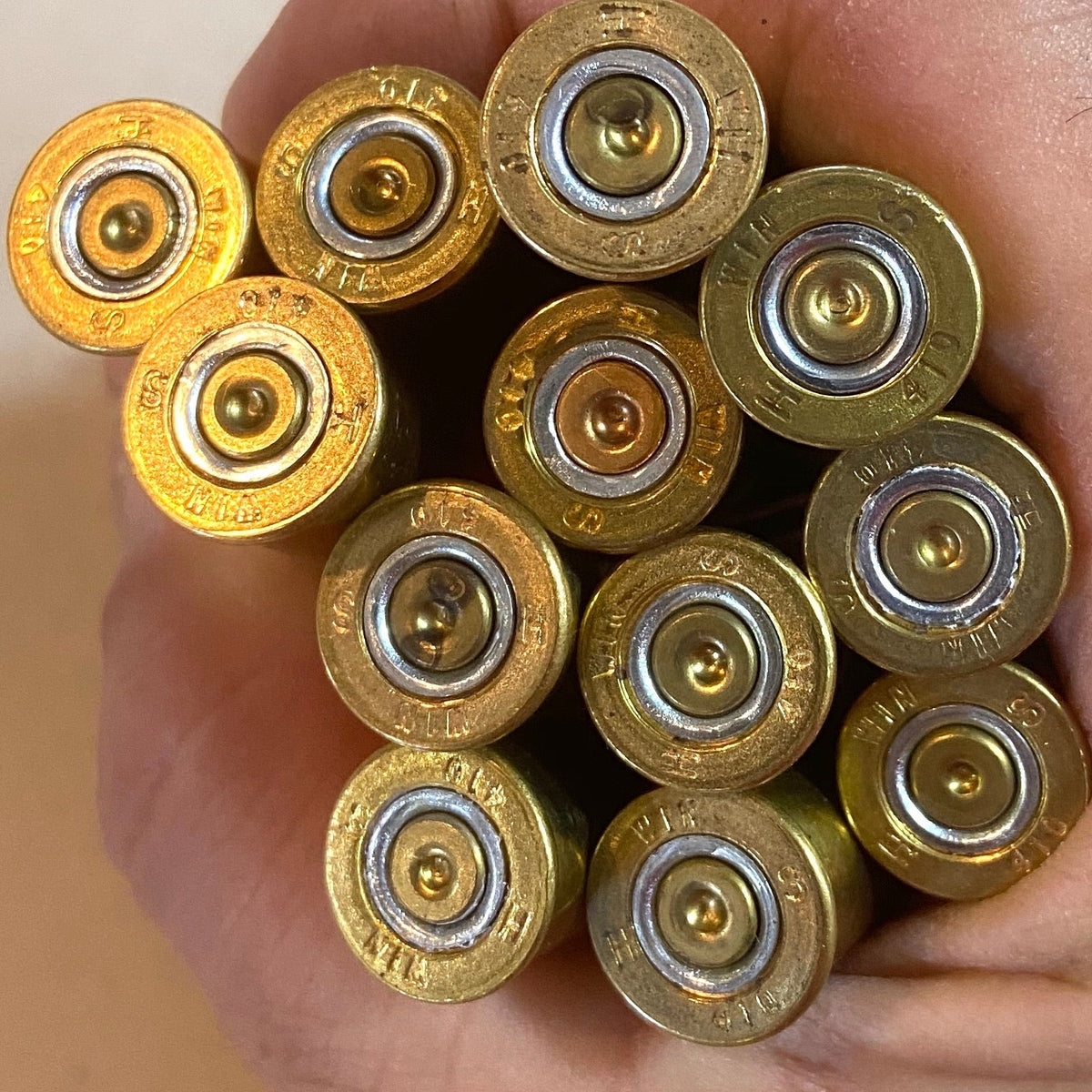 12 brass headstamp ends of Winchester AA 410 bore shotgun shells held in a hand