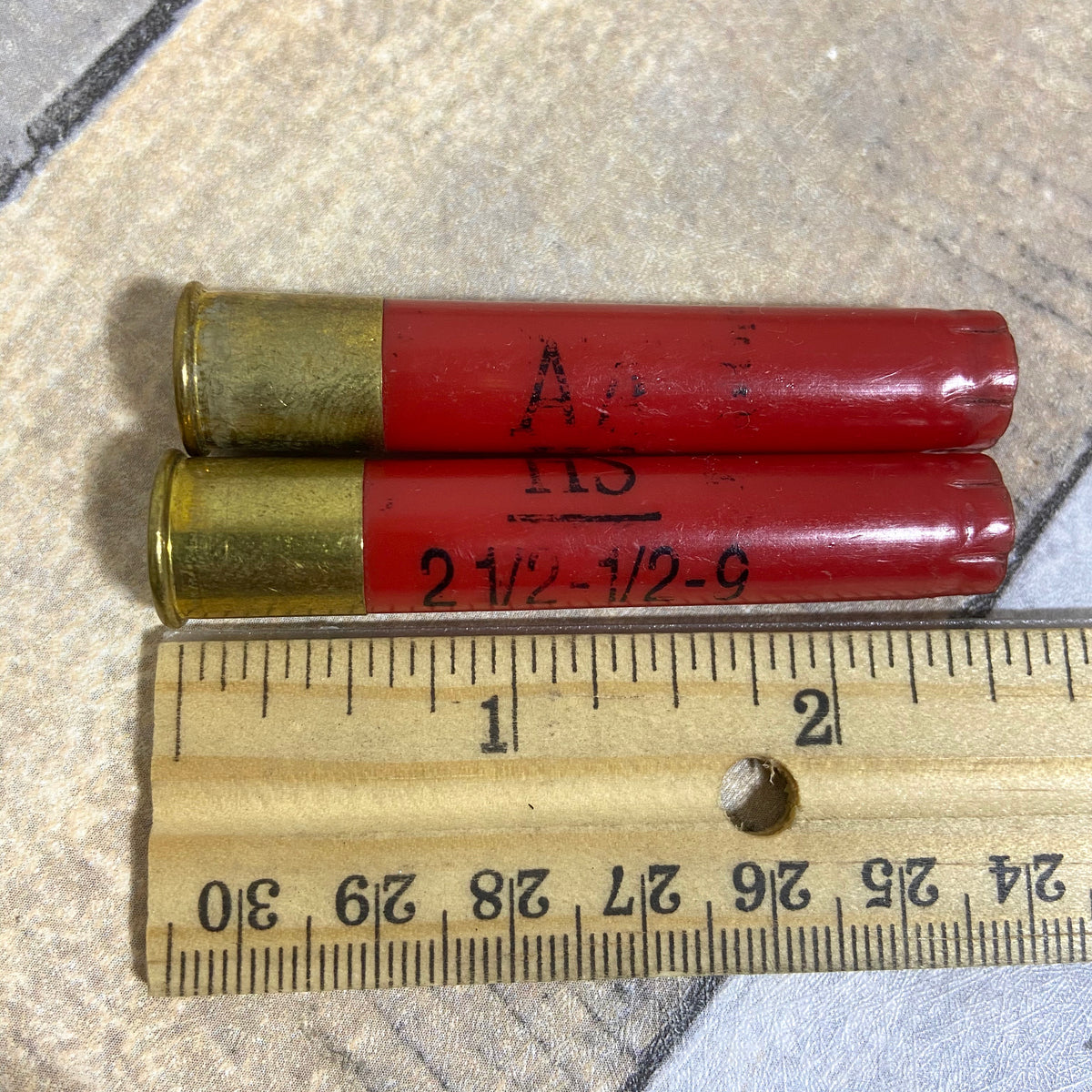 2 red Winchester AA 410 bore shotgun shell hulls marked AA and 2 1/2-1/2-9 next to a ruler