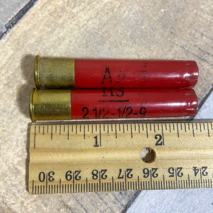2 red Winchester AA 410 bore shotgun shell hulls marked AA and 2 1/2-1/2-9 next to a ruler