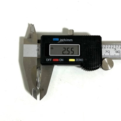 Digital caliper measuring the thickness of a Remington 12 gauge shotgun shell slice, held on edge between the jaws with a 2.55 reading on the display