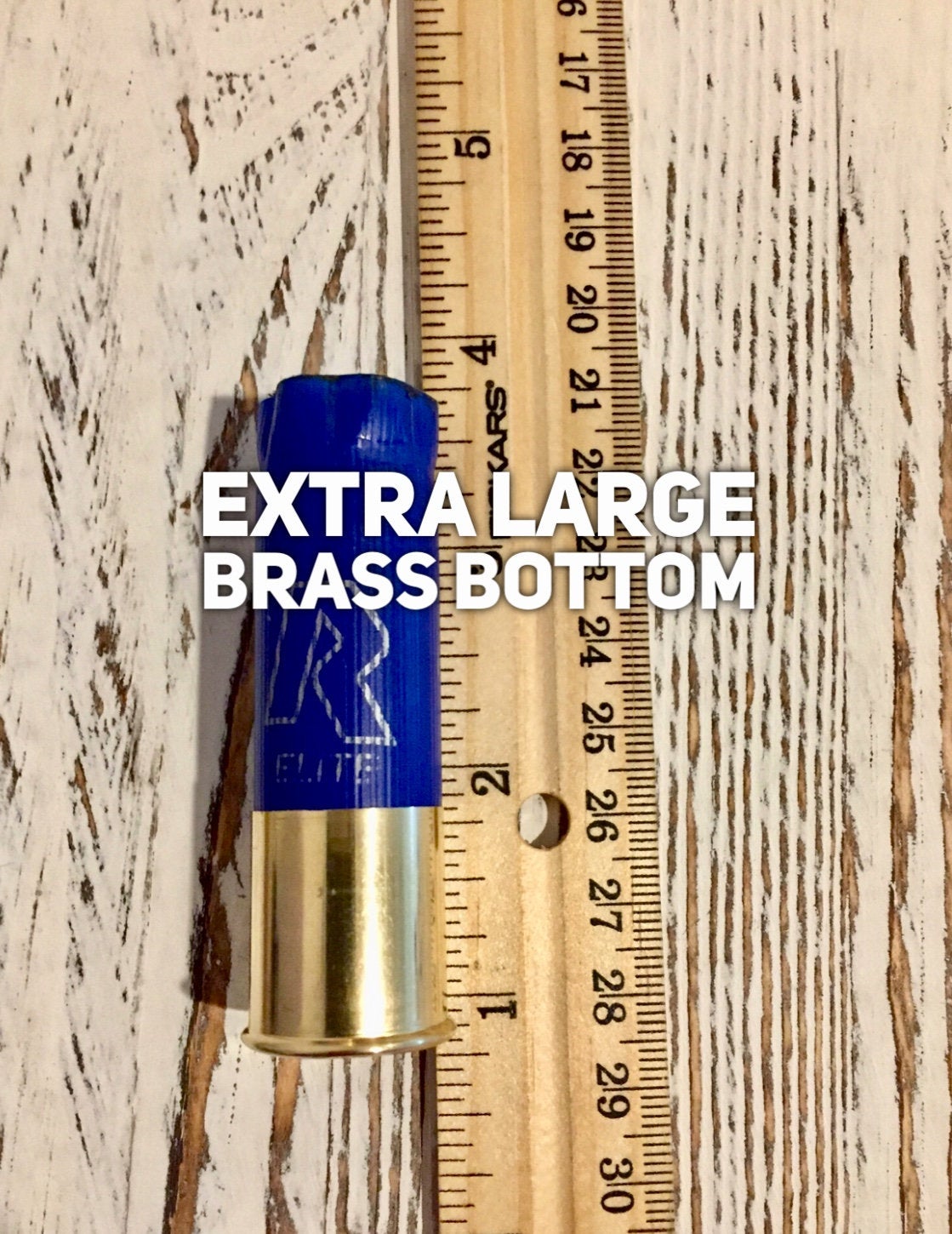 Single blue shotgun shell with an extra large brass base measured against a ruler, with ‘EXTRA LARGE BRASS BOTTOM’ text overlay