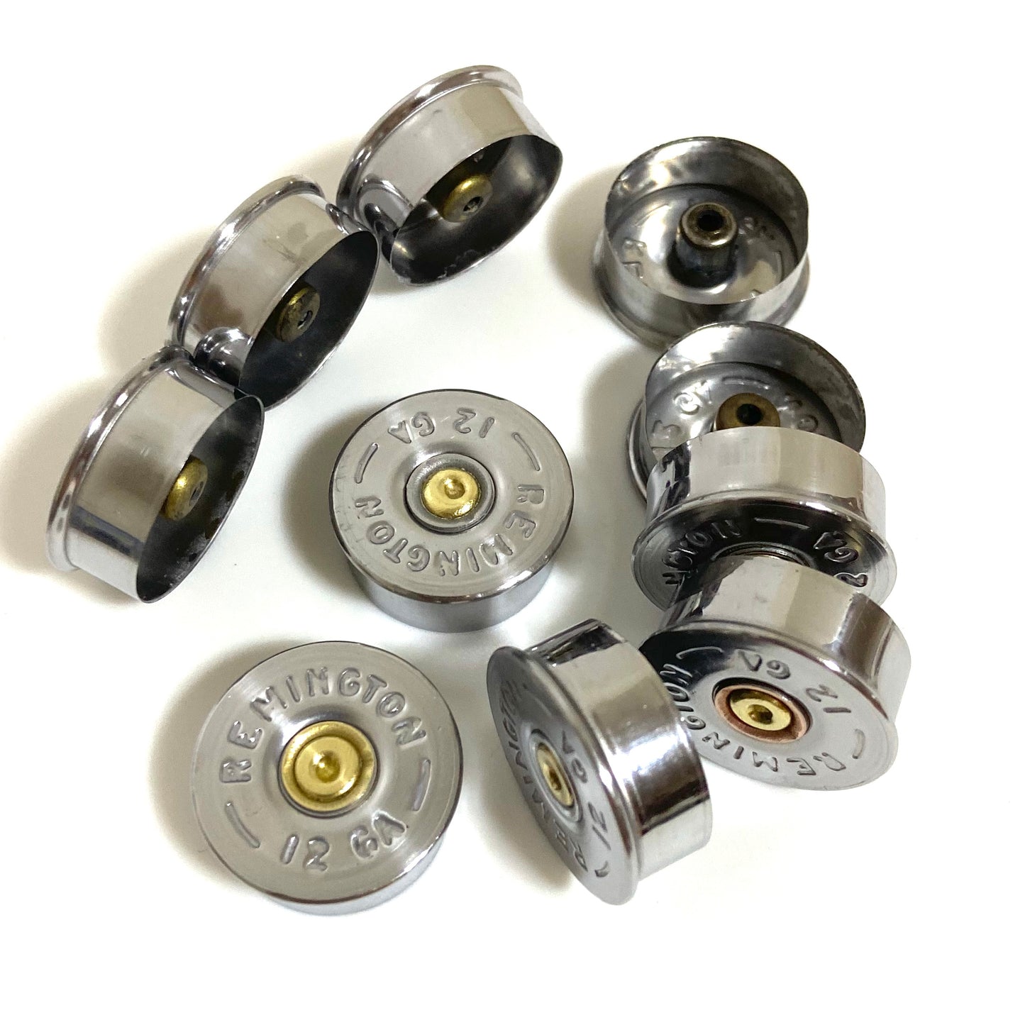 Eight  polished silver empty shotgun shell end caps on white background Remington displaying top bases and hollow interior undersides.