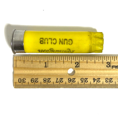 Single yellow Remington Gun Club 20 gauge shotgun shell resting on a wooden ruler, showing its length of about 2¾ inches from silver base to crimped top
