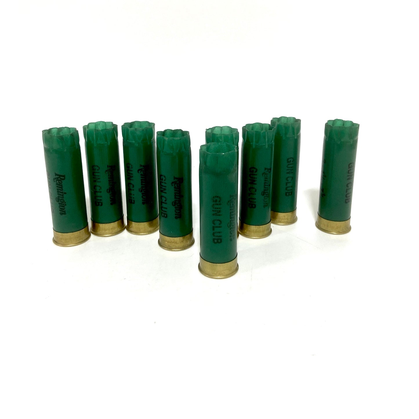Eight green Remington Gun Club 12 gauge empty shotgun shells with gold bases standing on a white background