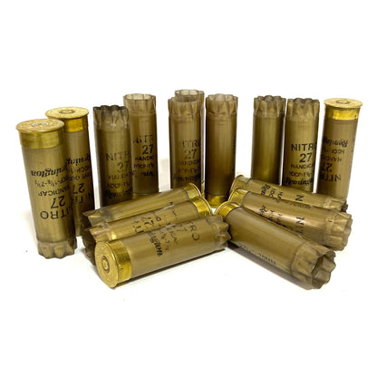 A cluster of gold Remington Nitro 27 shotshells wiped clean standing and lying on a white surface.