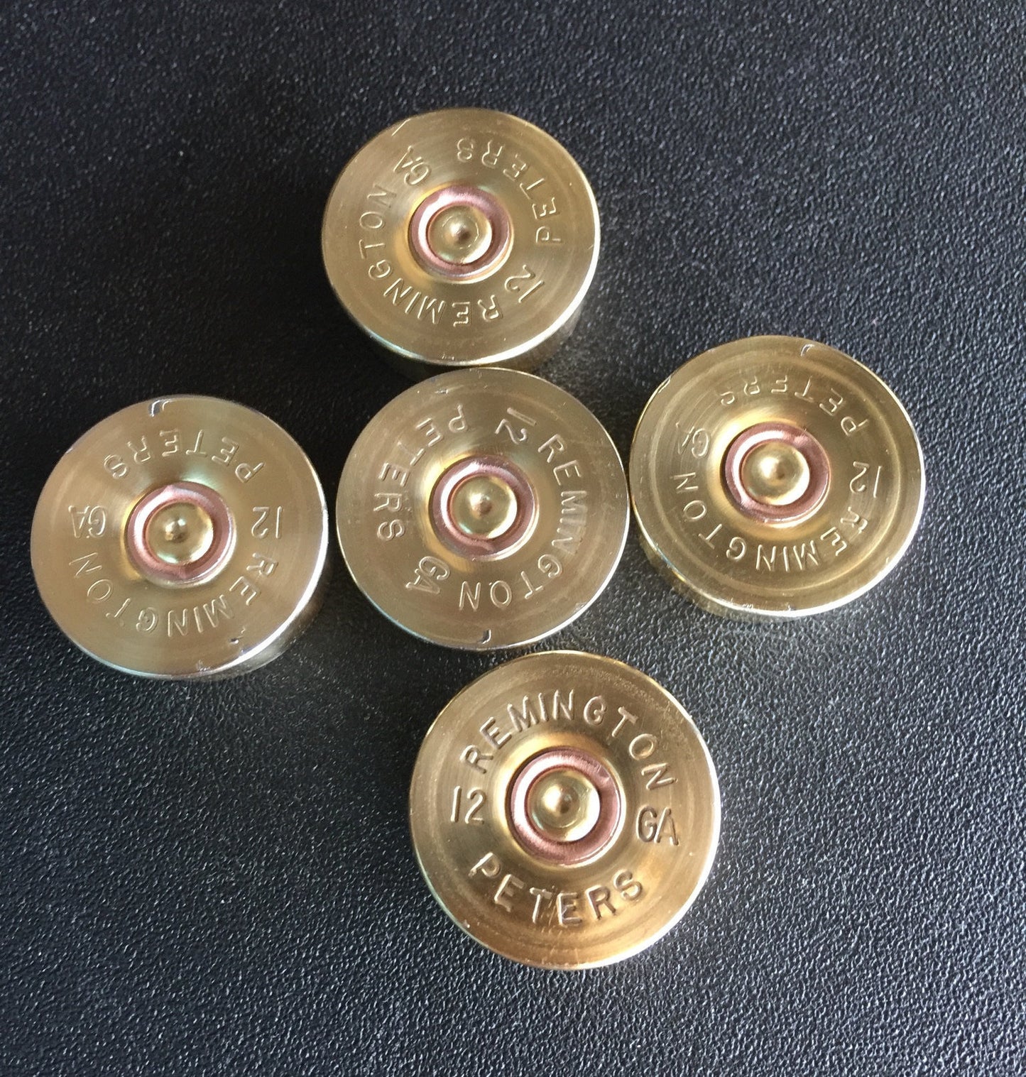 Five gold-toned Remington Peters 12 gauge shotgun shell headstamps arranged in a star pattern on a black background