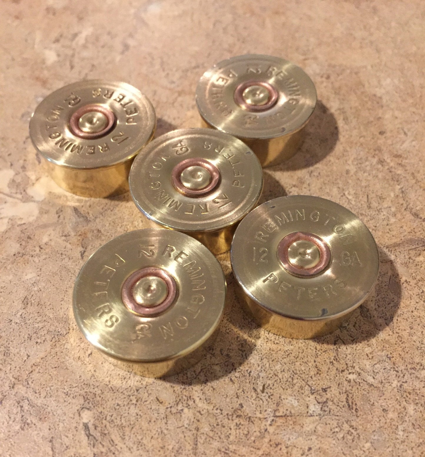 Five gold-toned Remington Peters 12 gauge shotgun shell headstamps arranged in a cluster on a stone countertop