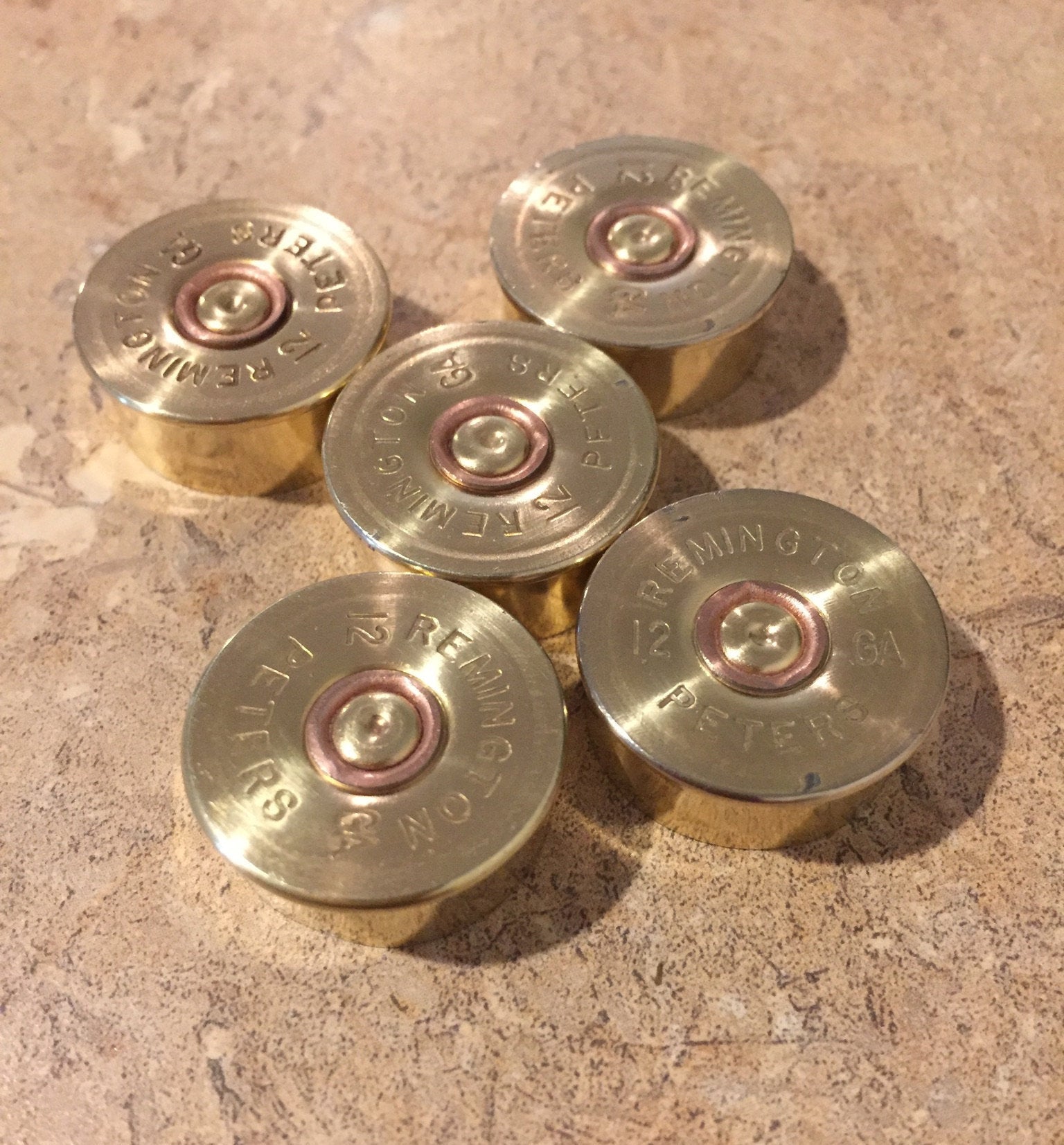 Five gold-toned Remington Peters 12 gauge shotgun shell headstamps arranged in a cluster on a stone countertop