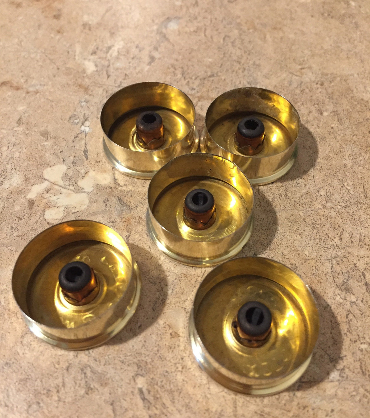 Five gold-toned Remington Peters 12 gauge shotgun shell headstamps viewed from the base, showing spent primers