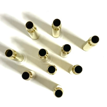 Several polished rifle shells standing upright in diagonal rows on a white surface, showing their open dark circular ends.
