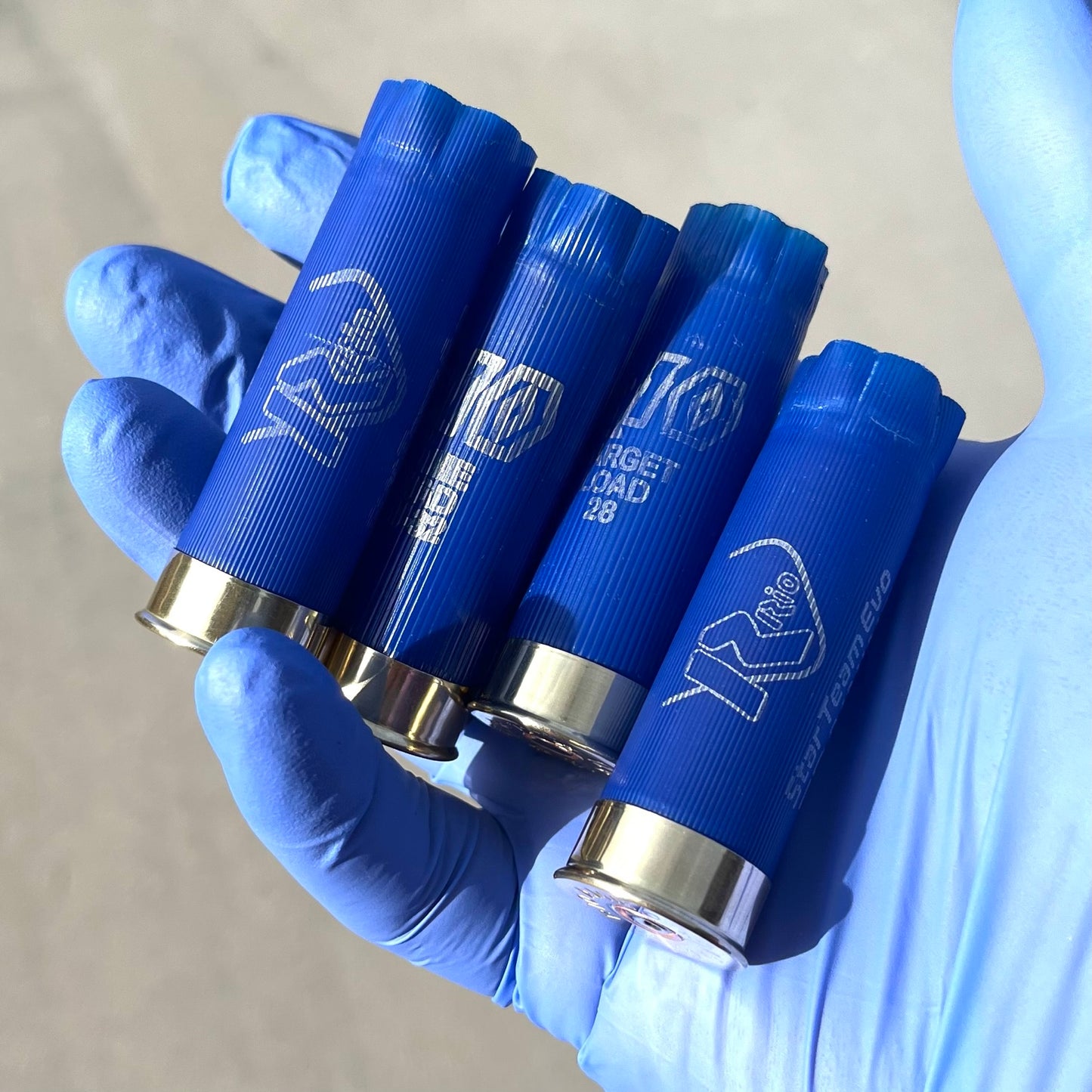 Four blue Rio 12 gauge shotgun shell hulls held in a gloved hand showing "Rio Star Team Evo" print