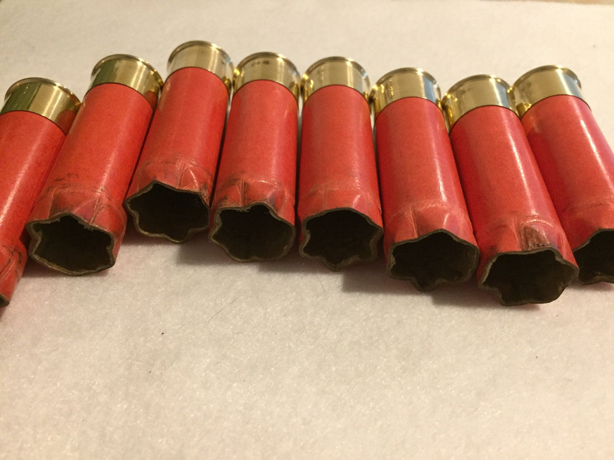 8 salmon pink paper shotgun shells lying in a row showing open mouths and gold brass heads