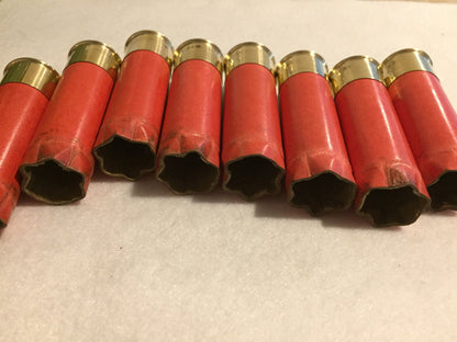 8 salmon pink paper shotgun shells lying in a row showing open mouths and gold brass heads