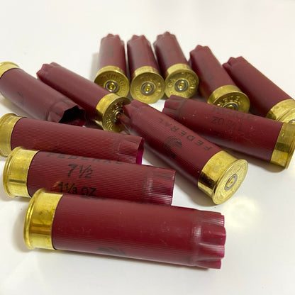 A scattered pile of dark red burgundy Federal 12 gauge empty shotshells on a white background.
