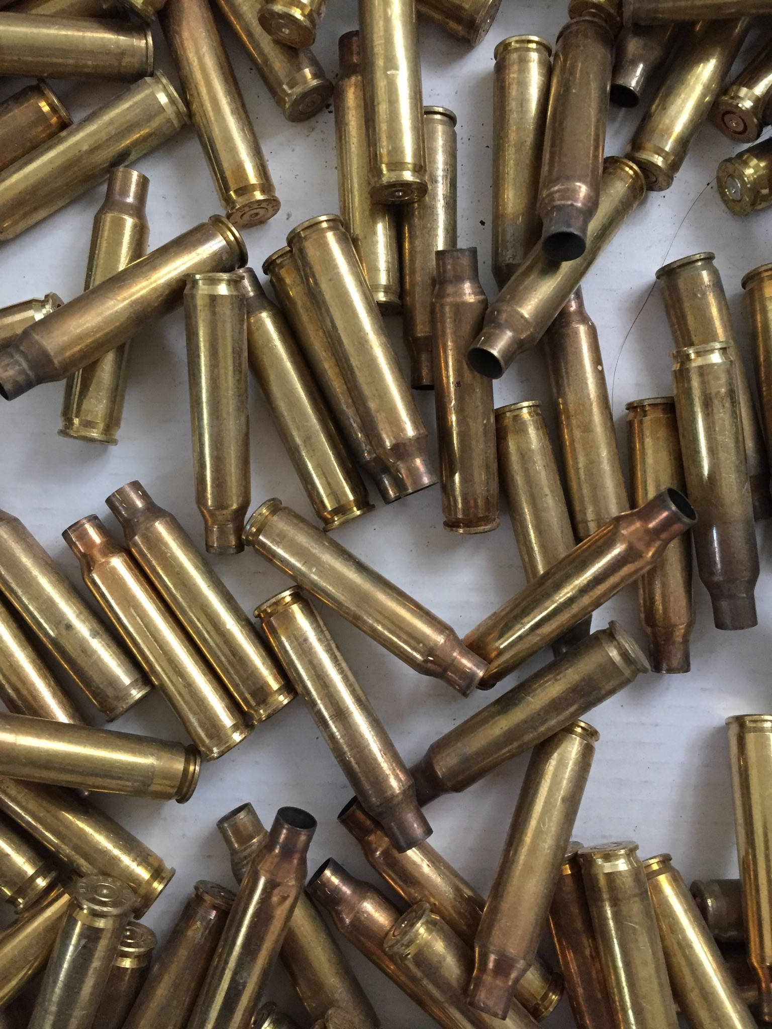 Large scattered pile of dirty .223 and 5.56 spent brass casings lying flat, displaying tarnished sides and empty necks.