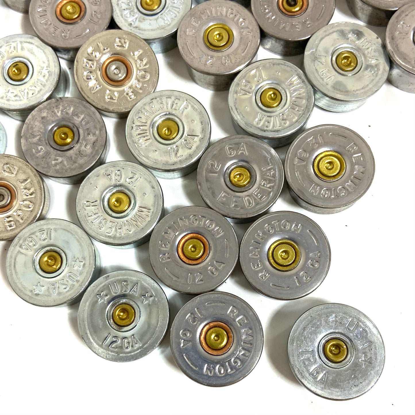 Silver 12 gauge shotgun shell bottoms loosely arranged on white, showing various manufacturer stamps.