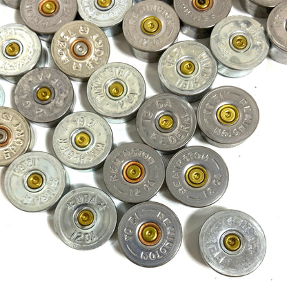 Silver 12 gauge shotgun shell bottoms loosely arranged on white, showing various manufacturer stamps.