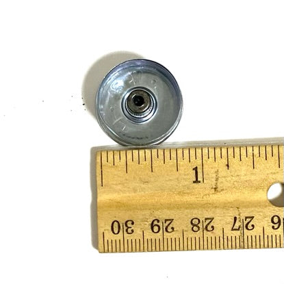 Silver 12 gauge shotgun shell headstamp shown from the inside, with a blue tarnish tone, beside a wooden ruler.