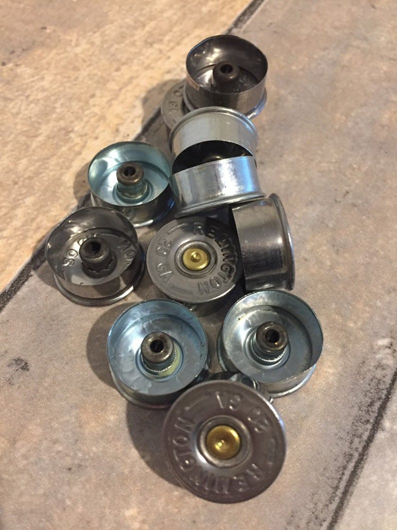 Ten silver 20 gauge shotgun shell brass end caps with Winchester and Remington headstamps on a tile floor