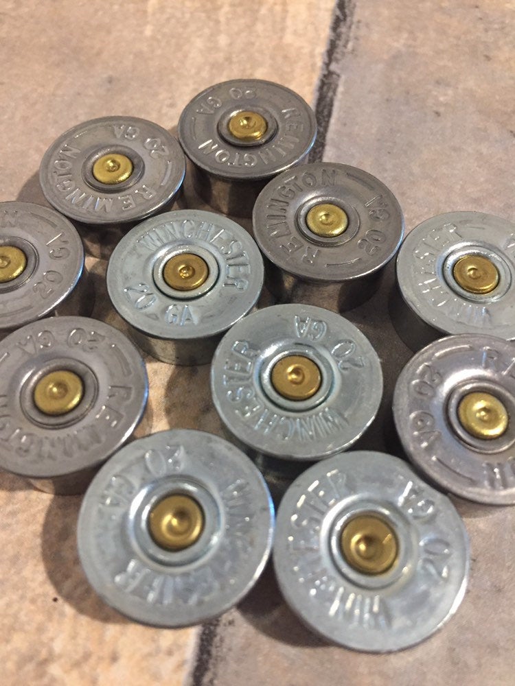 Ten silver 20 gauge shotgun shell brass end caps with Winchester and Remington headstamps arranged face up on a tile floor