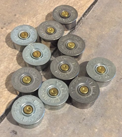 Ten silver 20 gauge shotgun shell brass end caps with visible headstamps arranged in a cluster on a tile floor