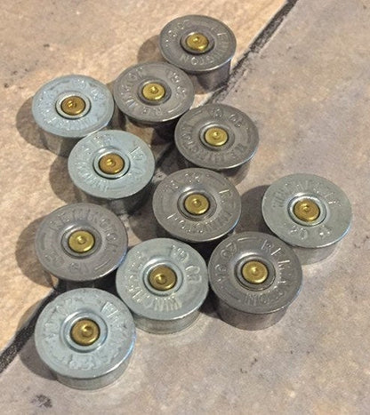 Ten silver 20 gauge shotgun shell brass end caps with visible headstamps arranged in a cluster on a tile floor
